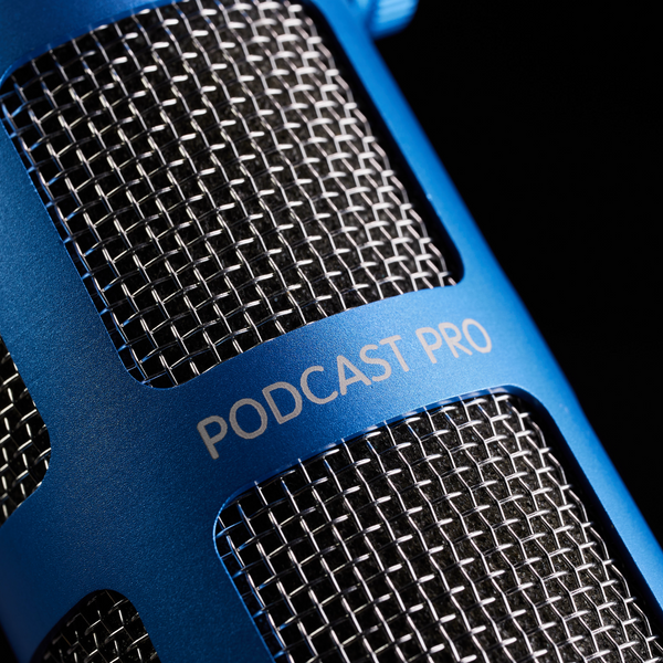 A close-up image on black background of a Sontronics Podcast Pro microphone in blue with the focus on the blue body casing, the laser-engraving 'Podcast Pro' logo, the stainless steel grille and the acoustic foam inside