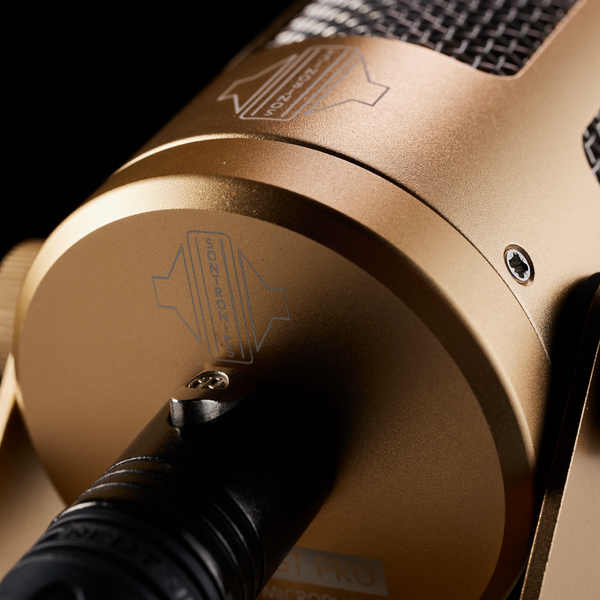 A close-up image on black background of a Sontronics Podcast Pro microphone in gold, showing the rear connected to an XLR cable and also showing the gold body casing with the Sontronics logo and the stainless steel grille