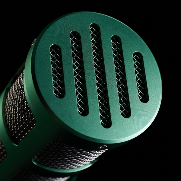 A close-up image on black background in dark light showing the Sontronics Podcast Pro microphone in green coming towards us, facing slightly to the right with the vintage-styled end grille in the foreground