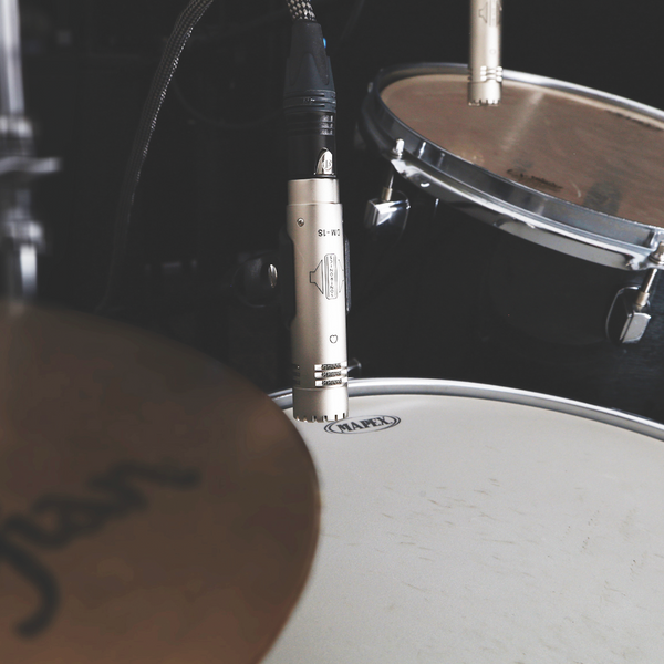 An image of a Sontronics DM-1S microphone mounting in its clip and pointing towards the surface of a Mapex snare drum. A Sontronics DM-1T microphone on a tom tom in the background anda glimpse of a Zildjian cymbal in the foreground