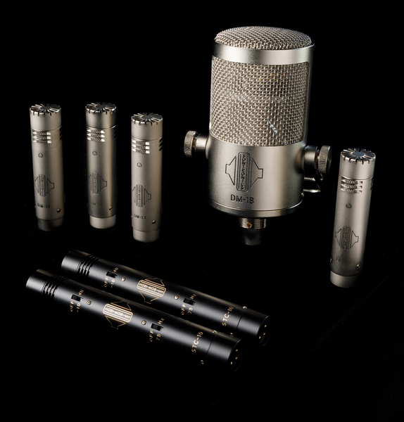An image on a black background showing five silver-coloured Sontronics mics standing up (three DM-1T tom mics, a large DM-1B mic and a small DM-1S mics) plus two black pencil-style STC-10. microphones lying down in the foreground 