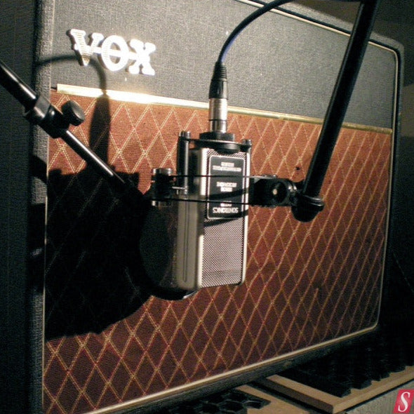 Image of a VOX AC30 guitar ampp with its recognisable brown grille cloth with diamond pattern, in front of which is suspended upside down from a microphone stand a Sontronics Delta microphone with a popshield between it and the amp front cloth