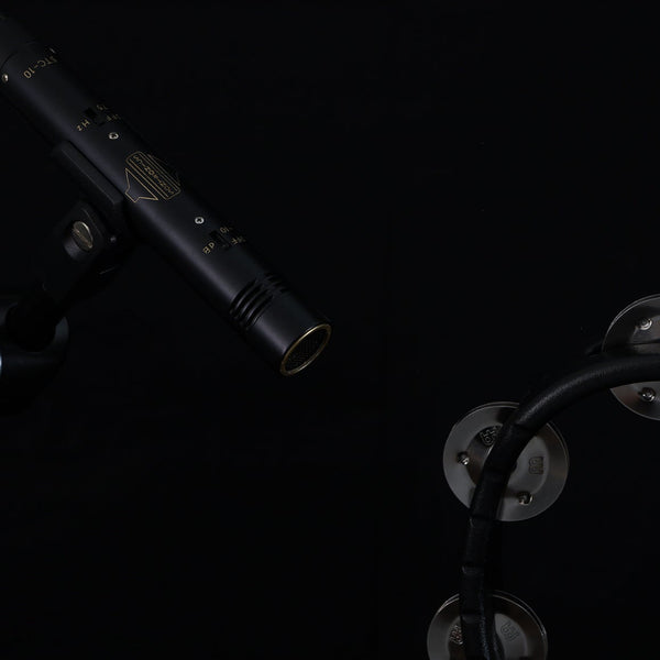 Image on black background of a black Sontronics STC-10 pencil style microphone on a mic clip coming in from the top left corner and pointing to the bottom right corner where we we the curve and bells of a black tambourine