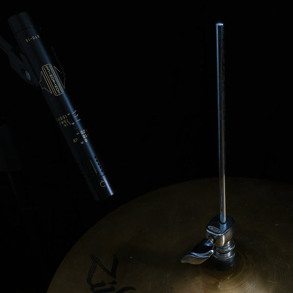 Image on black background of a black Sontronics STC-1 pencil style microphone suspended from above pointing downwards and to the right at a Zildjian hi-hat