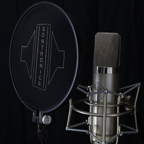 Image on black background of the circular black nylon mesh head of a Sontronics ST-POP popshield with the large white Sontronics logo on the left placed in front of a silver Sontronics Aria microphone